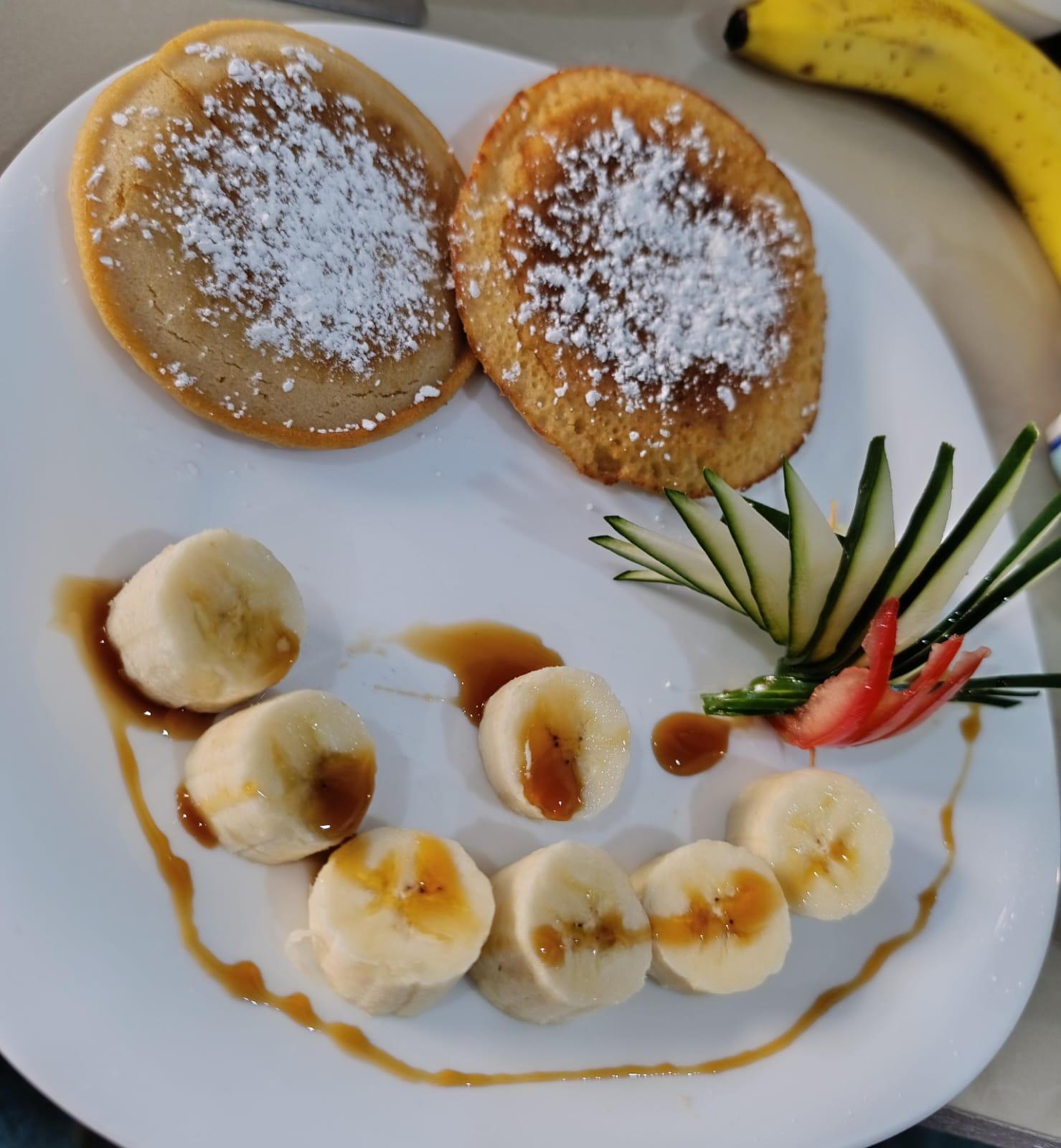 Fluffy pancakes with powdered sugar, fresh banana and caramel sauce for breakfast at Hotel Serendipity